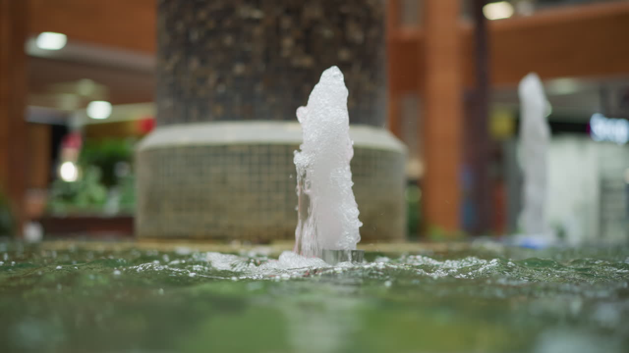 모자이크 타일로 된 기둥으로 둘러싸인 현대 쇼핑몰에서 활기찬 다채로운 불빛으로 조명 된 하천을 특징으로하는 물 분수