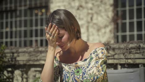 sad young woman weeping and holding hand on head outdoors in sunlight, portrait close up