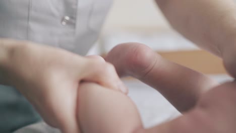 pediatra experto sostiene en las manos pequeñas piernas masajeando
