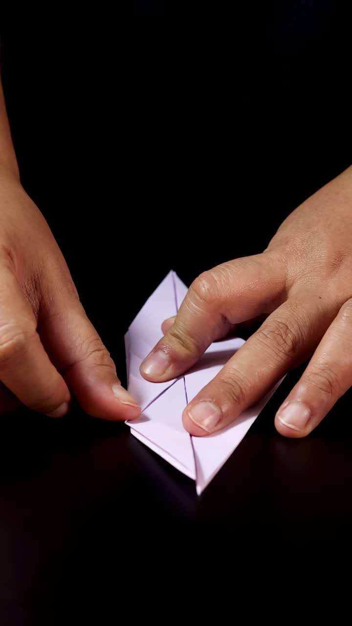 Mani adulte piegano con cura carta bianca per creare un uccello origami, vista dall'alto, illuminazione da studio.