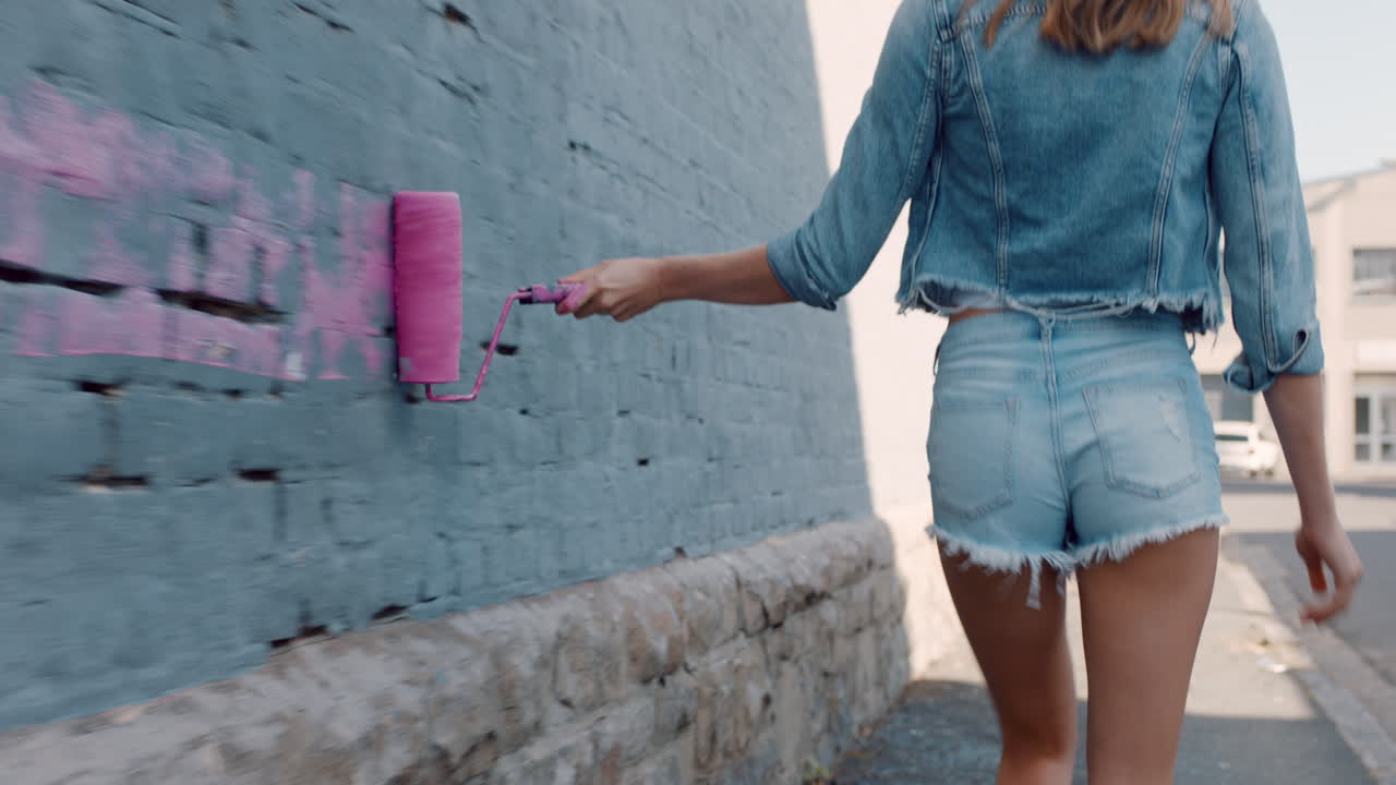 hermosa mujer artista pintando la pared con pintura rosa caminando por la calle de la ciudad confiada mujer rebelde disfrutando de la expresión artística con el arte de graffiti urbano