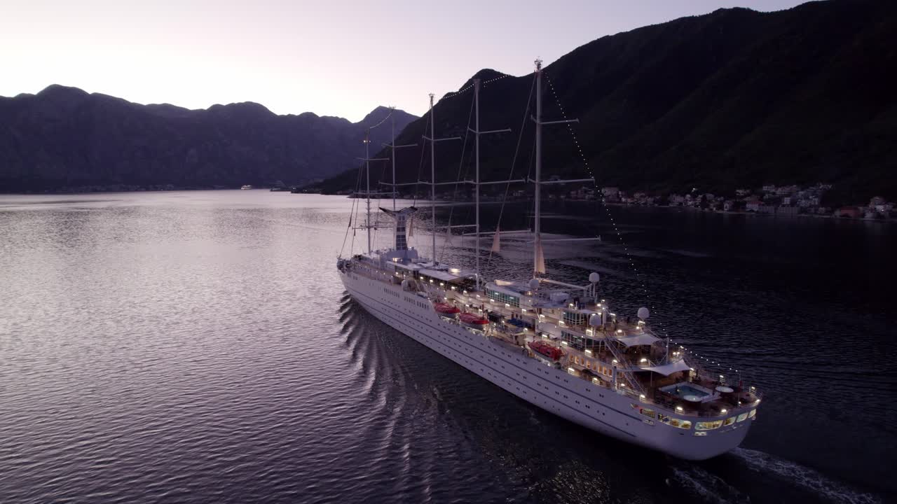 Flygfoto över kryssningsfartyg som seglar genom Kotorbukten vid soluppgången i Kotor, Montenegro, med fantastiskt soluppgångsljus, lugn atmosfär och högkvalitativ drönarfilm som avslöjar fridfulla vyer.
