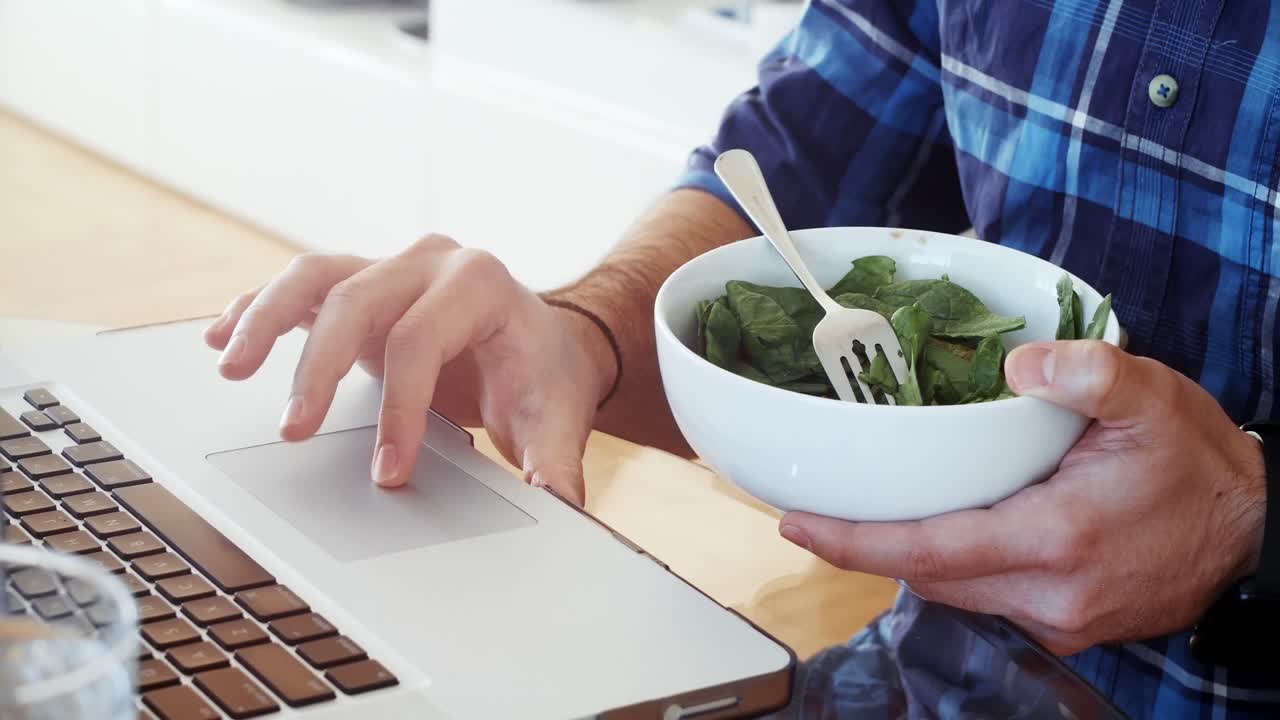 hombre desayunando mientras usa una computadora portátil en casa 4k