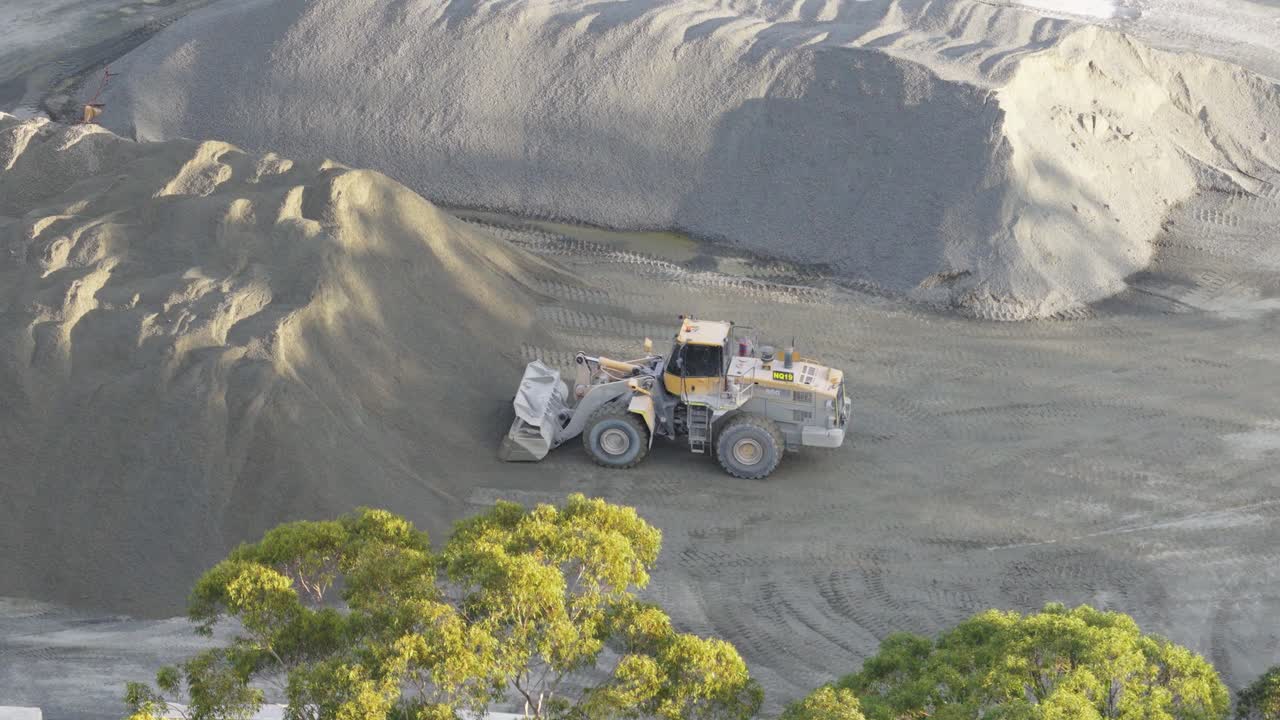 Drone footage captures a utility vehicle moving soil in a Gold Coast quarry under natural daylight