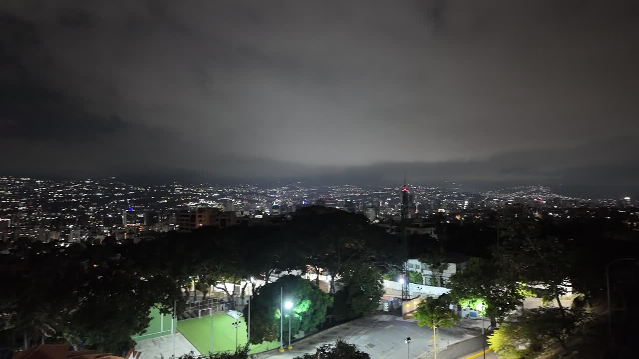 Panoramic night view of Caracas from a viewpoint with glowing city lights and trees
