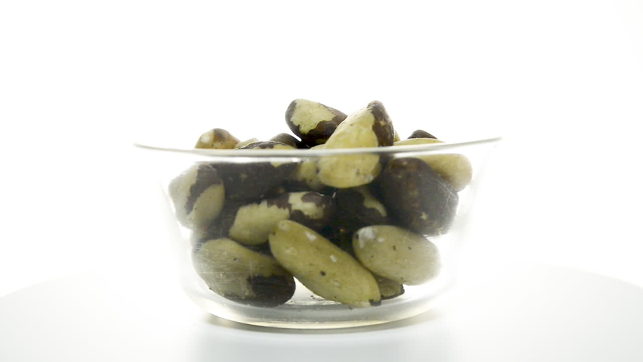 tazón de vidrio transparente con nueces de brasil girando sobre un fondo blanco