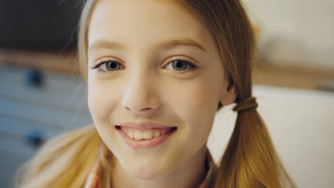 Portrait-shot-of-the-lovely-pretty-teen-girl-with-long-blonde-hair-in-two-tails-looking-straight-to-the-camera.-Close-up.-Indoor