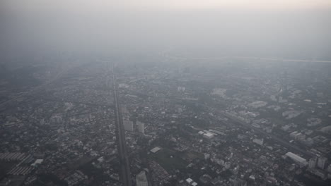 passenger view from the inside of a flying plane push in and pull out of the window with view of a modern city surrounded by fog and pollution