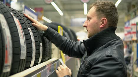 Junger-Mann-Blickt-In-Der-Automobilabteilung-Des-Hypermarkts-Auf-Autoreifen-Und-Versucht,-Eine-Auswahl-Zu-Treffen