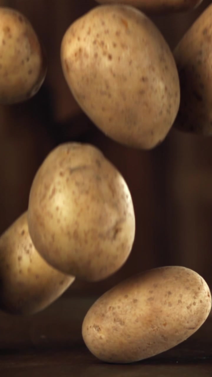 Patate fresche crude che cadono al rallentatore su sfondo scuro