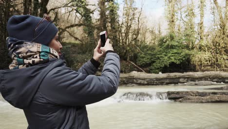 person taking photo of a waterfall in a forest