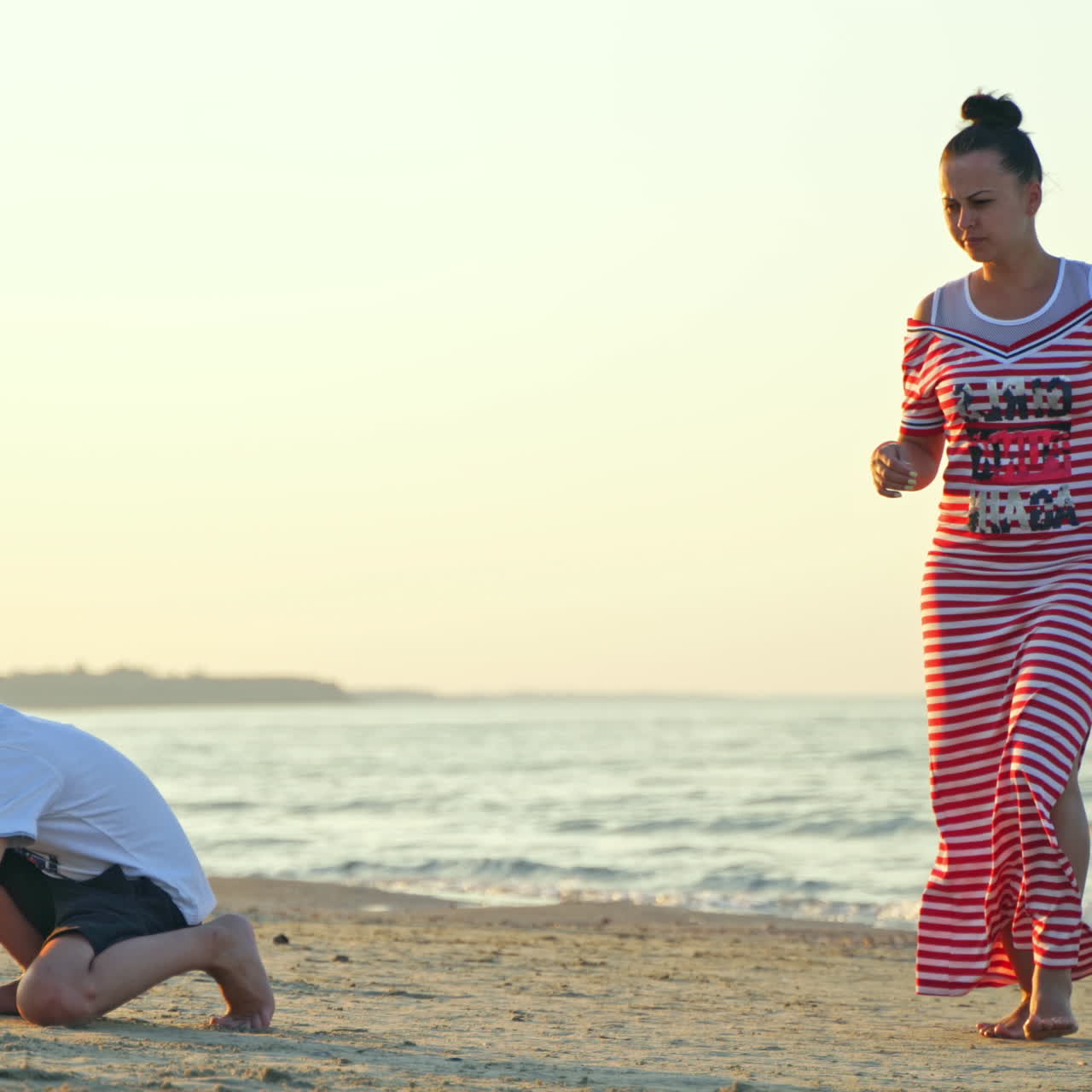 Woman and a boy on the seacoast. Mother in long dress is having good time with her son together on the sand beach during summer holidays.