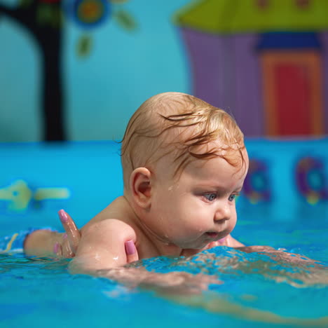 blond caucasian baby boy is held in water by woman. cute kid moves his hands in water making splashes.