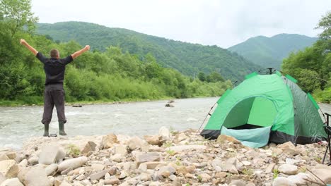 male happy tourist by the river in middle of the mountains male happy tourist by the river in the middle of the mountains beautiful landscape summer landscape ecological tourism privacy and travel concept