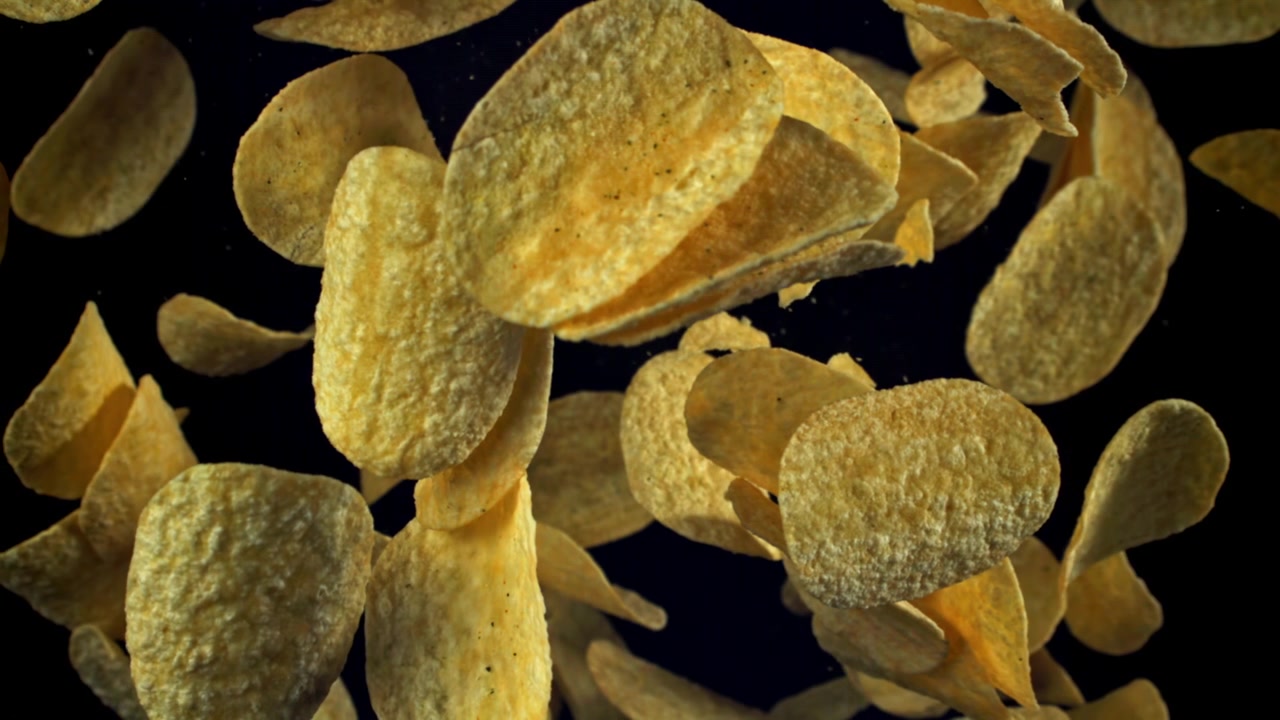 Golden Potato Chips Falling in Slow Motion on Black Background