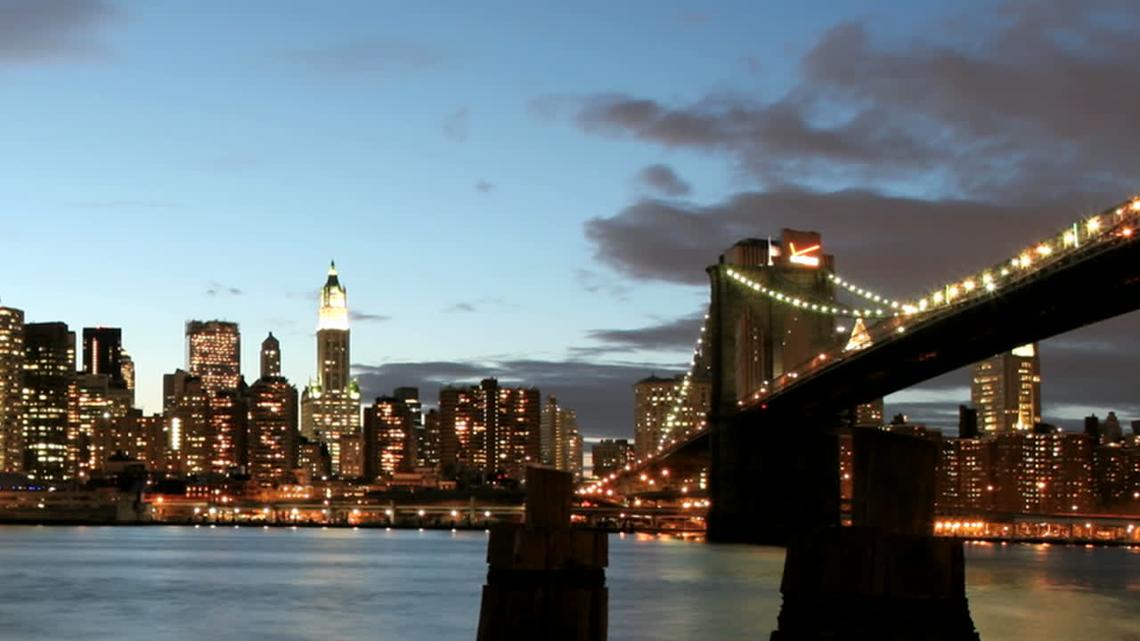 Panoramica lenta di una vista in timelapse del Ponte di Brooklyn e dello skyline di New York City dall'ora d'oro alla notte.