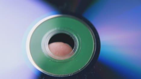 man holds shining compact disc on finger in dark background