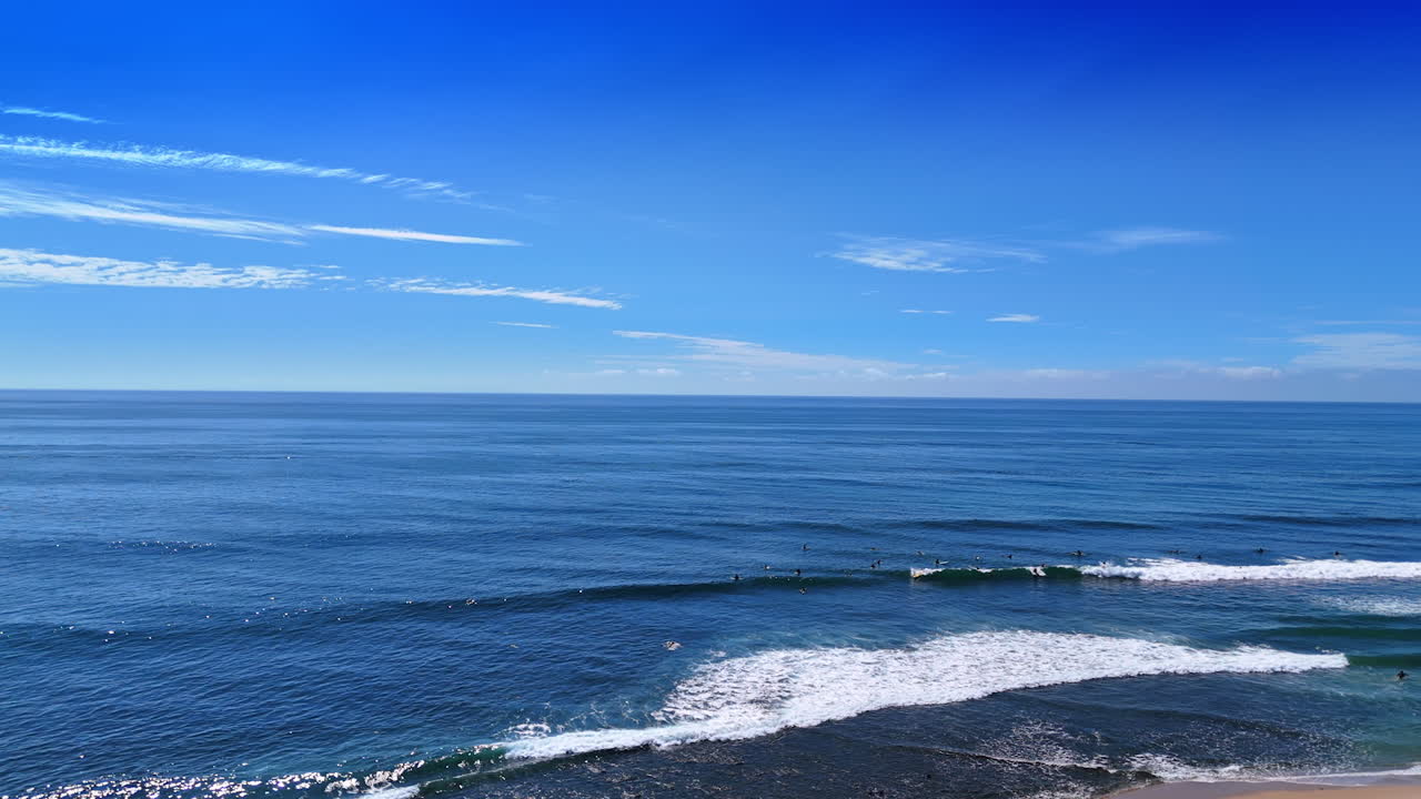 White foamy waves roll to the coast. Surfers are practicing in the Pacific Ocean on sunny day. Malibu, California, USA. Aerial view