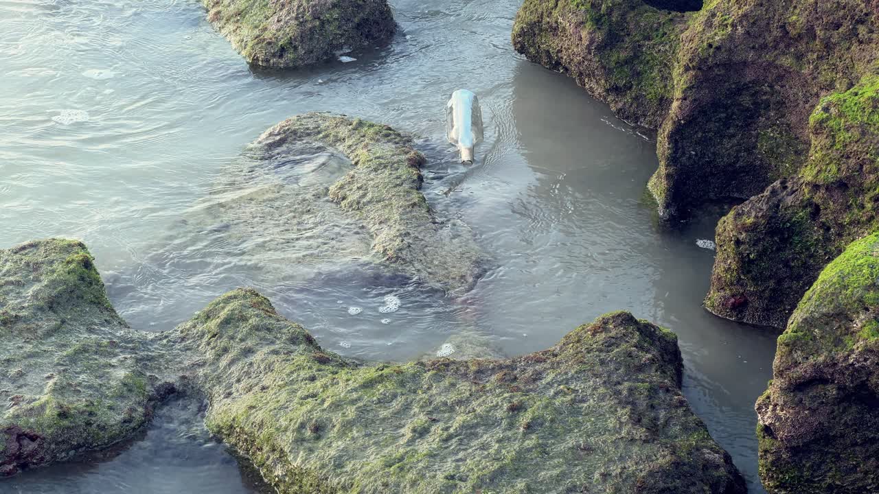 una botella entre las rocas en una playa de arena siendo sacada al mar