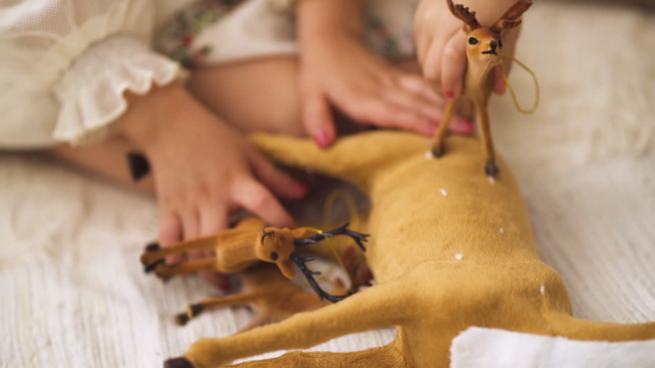 Rallentatore di una bambina in abito natalizio che gioca con statuette giocattolo di cervi - Primo piano