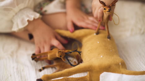 cámara lenta de niña en vestido de navidad jugando con figuritas de juguete de ciervo - primer plano