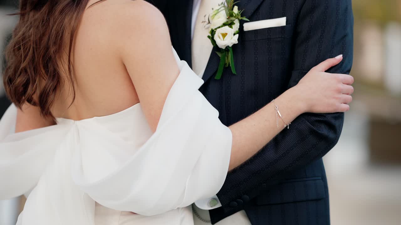 Bride embracing groom in wedding attire with boutonniere visible