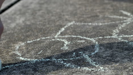 close up of young boys hand drawing a cat on cement driveway