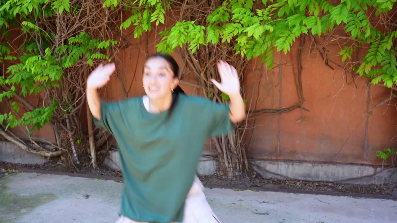 Woman dancing outdoors by a wall with a tree