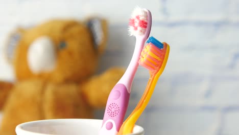 cepillos de dientes de niños coloridos en una taza con un oso de peluche