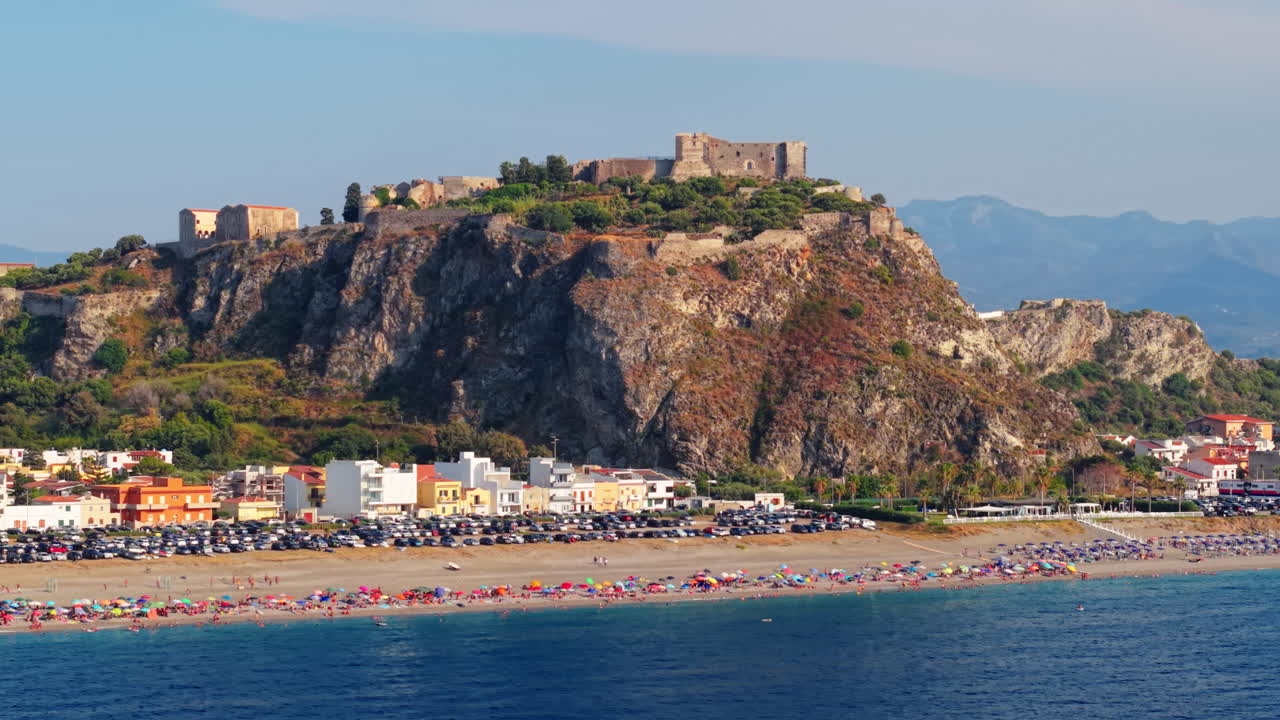 Vista aérea de praia com guarda-sóis vibrantes ao lado de falésia e cidade no verão