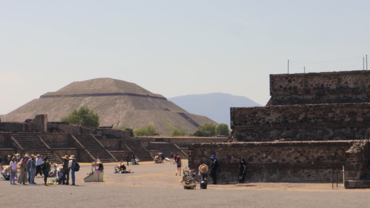 una amplia toma de seguimiento de la zona arqueológica de teotihuacan en méxico, con la pirámide del sol y otras ruinas al fondo, en un día claro y soleado con turistas caminando
