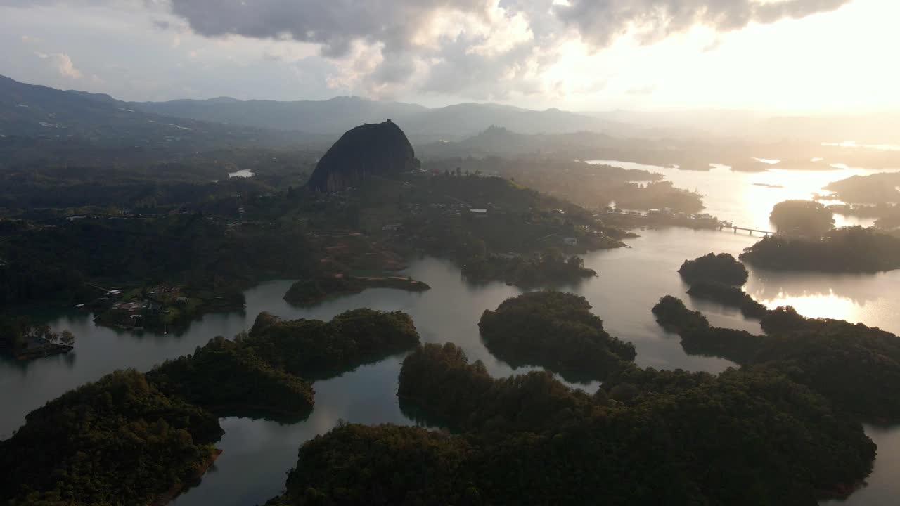 Aerial of Stone of Guatapé overlooking water at sunset, warm tones and serene reflections on calm waters