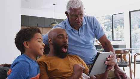 Familia-Afroamericana-Masculina-Multigeneracional-Sentada-En-Un-Sofá-En-Casa-Usando-Una-Tableta-Digital