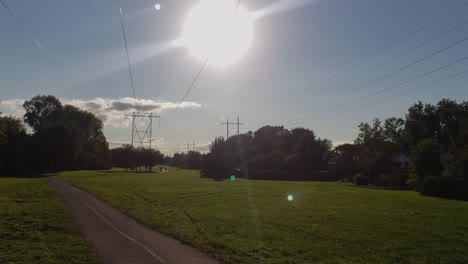 plano general de un sendero con ciclistas y caminantes en un día de verano con enormes líneas eléctricas encima y el sol a lo lejos