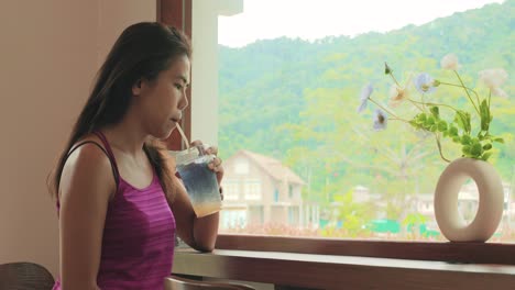 beautiful thai woman drinking a soda drink at a café bar window overlooking khao yai national park, thailand