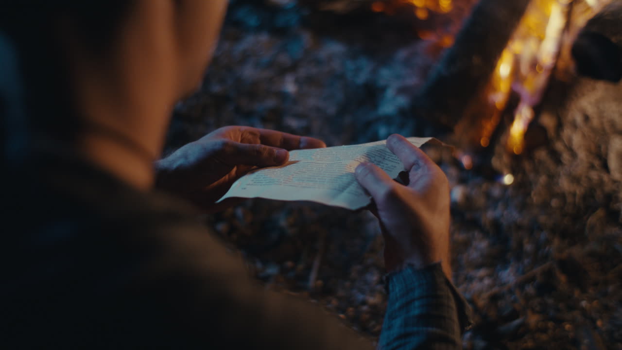 A person's hands interacting with a paper by a campfire at night