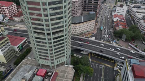 Drohne-Fliegt-über-Eine-Autobahn-Mit-Starkem-Verkehr-In-Kuala-Lumpur,-Malaysia-–-Vogelperspektive-Auf-Die-Straße-Neben-Einem-Wolkenkratzer