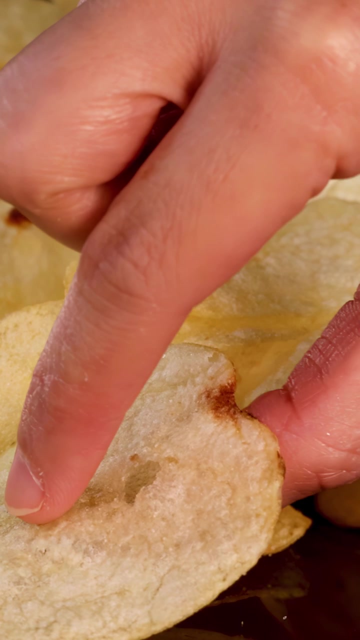 Una mano umana si avvicina e afferra patatine fritte sotto una luce intensa, prospettiva macro, sfondo nero.
