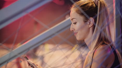 Confident-Beautiful-Young-Sporty-Woman-Using-Mobile-Phone-During-Break-At-Health-Club