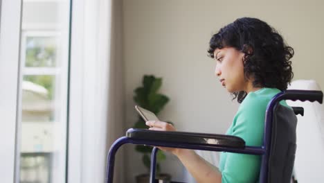 Una-Mujer-Discapacitada-Birracial-Pensativa-En-Silla-De-Ruedas-Usando-Una-Tableta-En-La-Sala-De-Estar