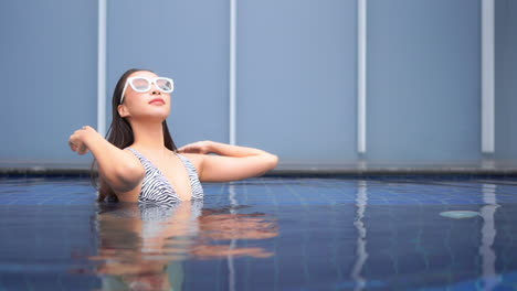 joven y atractiva mujer asiática arreglándose el pelo mojado en la piscina, concepto de productos de peluquería y cuidado del cabello, cámara lenta de cuadro completo con espacio de copia