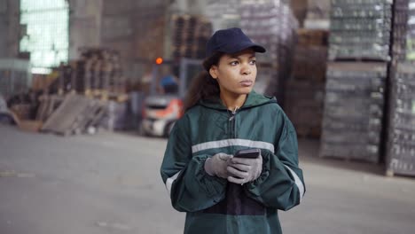 and-african-american-woman-in-a-special-green-uniform-is-chatting-on-the-phone-at-a-waste-recycling-plant.-Factory-background