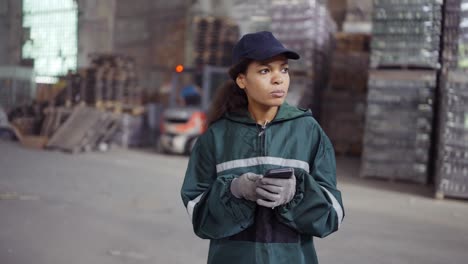 y una mujer afroamericana con un uniforme verde especial está hablando por teléfono en una planta de reciclaje de residuos.