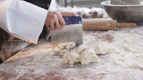 panadera asiática trabajando en la cocina de la panadería, cortando la masa en el mostrador en cámara lenta