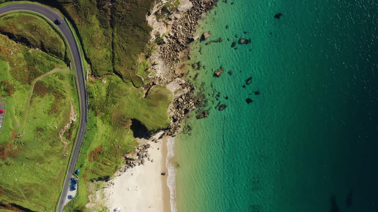 Aerial top down flight over Keem Beach coastal road with rugged cliffs and cars driving on Achill Island