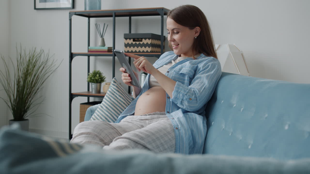 Pregnant woman using a tablet on a sofa