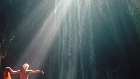 dancing woman in waterfall cave splashing water wearing beautiful dress enjoying nature dance feeling spiritual freedom 4k