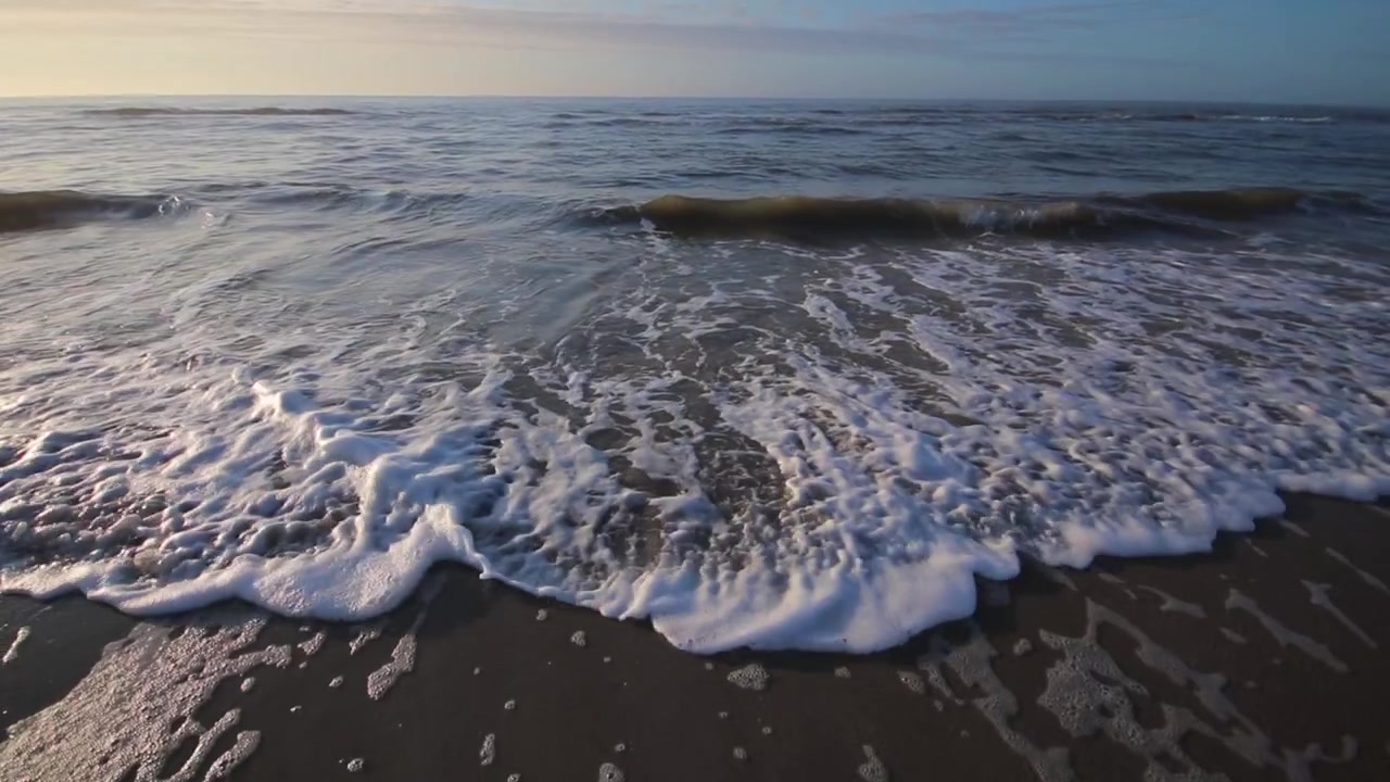 Onda che si infrange e risale la riva della spiaggia. L'acqua si riversa sulla sabbia e risale la battigia. Movimento lento.