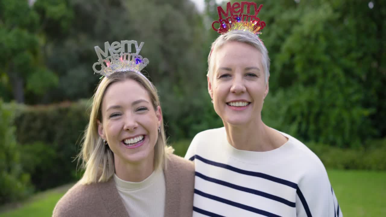 Madre e figlia che entrano in giardino indossando cerchietti con scritto «Buon Natale» mentre ridono e posano per una foto