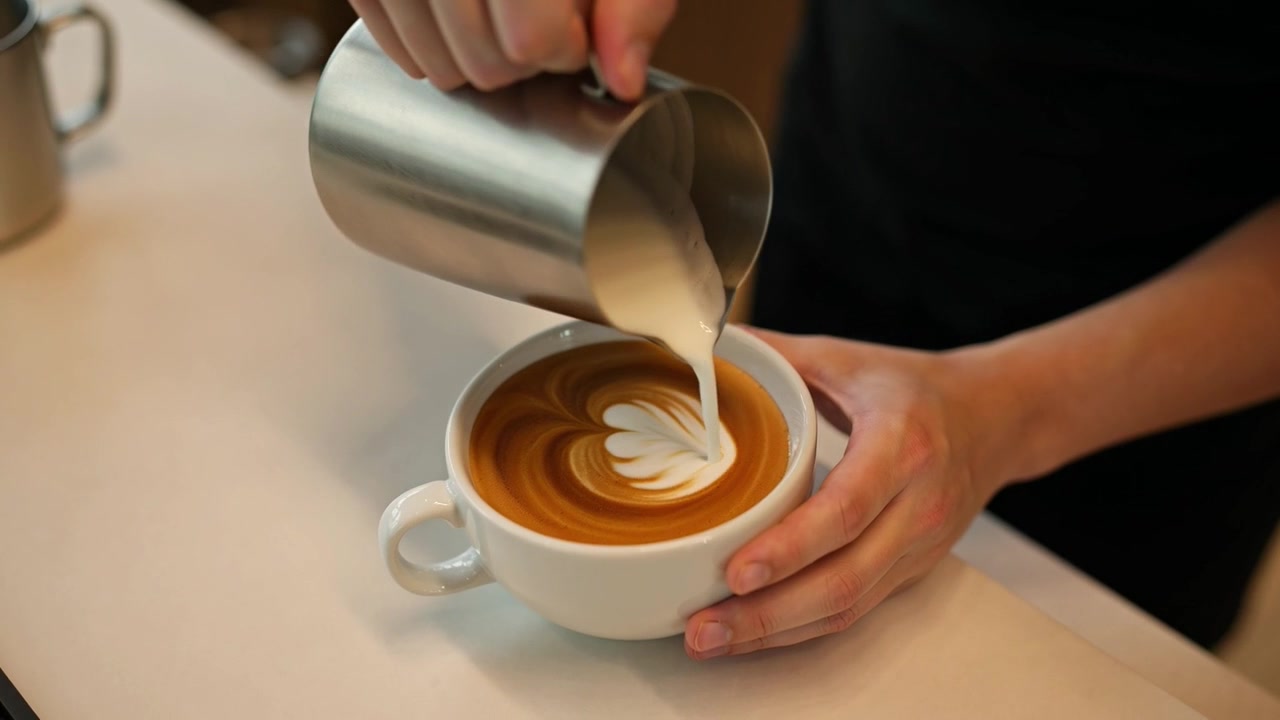 Barista che versa latte montato a vapore per creare latte art in una caffetteria